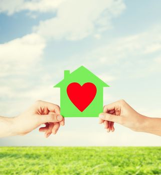 charity, real estate and family home concept - isolated picture of male and female hands holding green paper house with red heart