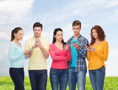 friendship, technology, nature and people concept - group of serious teenagers with smartphones over blue sky and grass background