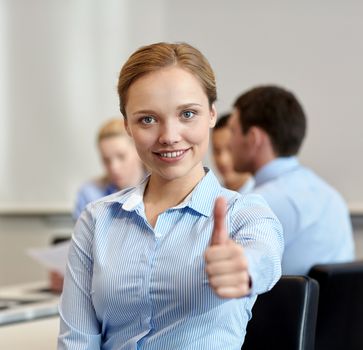 business, people, gesture and teamwork concept - smiling businesswoman showing thumbs up with group of businesspeople meeting in office