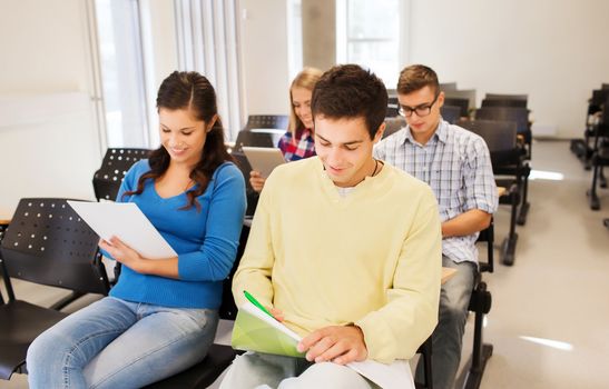 education, high school, teamwork and people concept - group of smiling students with notepads sitting in lecture hall