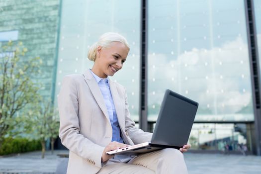 business, education, technology and people concept - smiling businesswoman working with laptop computer on city street