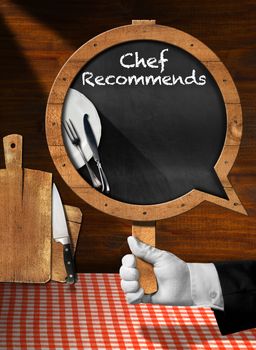 Hand of chef with white glove holding a pole with empty blackboard in the shape of speech bubble with text Chef Recommends