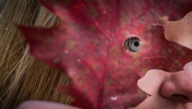 A young woman peers through a hole in a leaf.