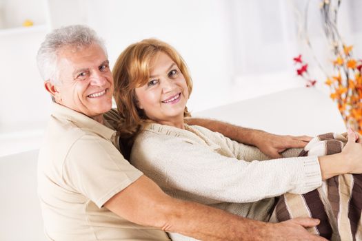 Hugging Senior couple sitting in living room.