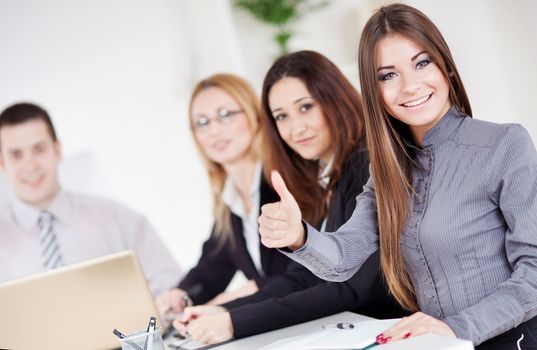 Happy Businesswoman showing thumbs up in the office. Looking at camera.