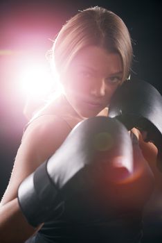 Portrait of Young beautiful boxing girl standing with a guard ready to punch. Black background with direct light with lens flare.