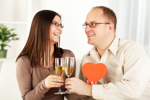 Happy Young couple in home interior enjoying in glass of champagne, with heart shaped box. The valentine's day.