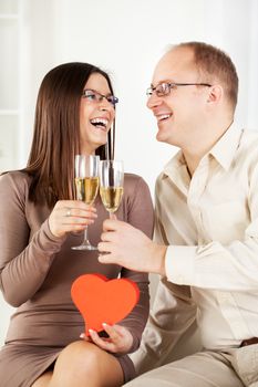 Happy Young couple in home interior enjoying in glass of champagne, with heart shaped box. The valentine's day.