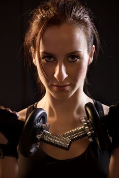 Portrait of a beautiful woman exercising with dumbbells on black background.