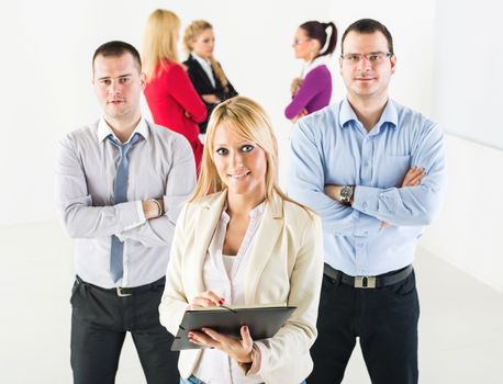 Three smiling co-workers standing in the office in front of their colleague. They are looking at camera.