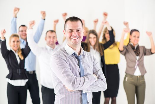 Successful and Smiling businessman with crossed arm standing in front of happy colleagues and looking at the camera.