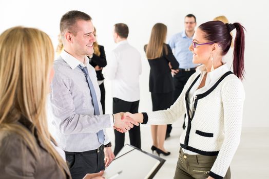 Successful business people shaking hands at the meeting because of Successful Agreement with coworkers standing in background. 