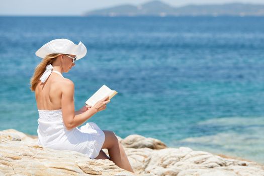 Young beautiful woman reading book and relaxing on the beach.