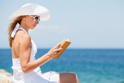 Young beautiful woman reading book and relaxing on the beach.