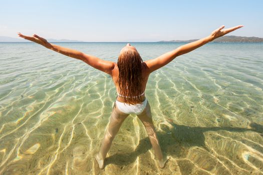 Young beautiful woman enjoying the sun and standing in transparent sea.