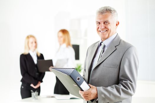 Happy senior businessman with documents standing in the office. Looking at camera. Selective Focus.