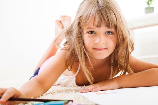 Cute little girl with color crayons lying on the floor