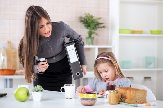 Overworked Mother Rushing her little daughter in the morning to go faster because she late for work. Daughter having breakfast. Mother and Daughter getting angry with each other because of stress.