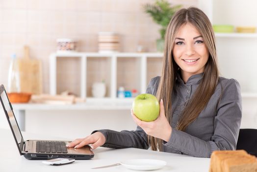 Businesswoman in the kitchen with apple reading mail on laptop before going to work.