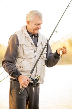 Senior Fisherman holding fishing rod with fish on the hook.