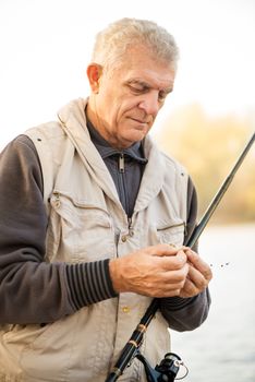 Senior Fisherman hooks a worm on a fishing hook.