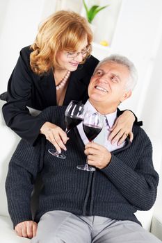 Happy Senior couple in home interior enjoying in glass of wine.