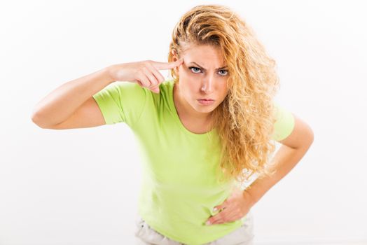 Angry young woman standing against a white background with a finger pressed against the head.