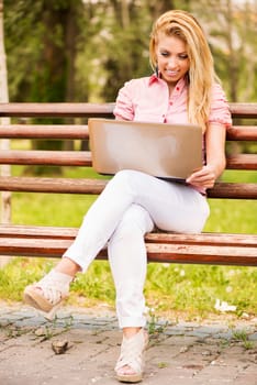 Young Beautiful Woman sitting and relaxing on the Park Bench and using laptop.
