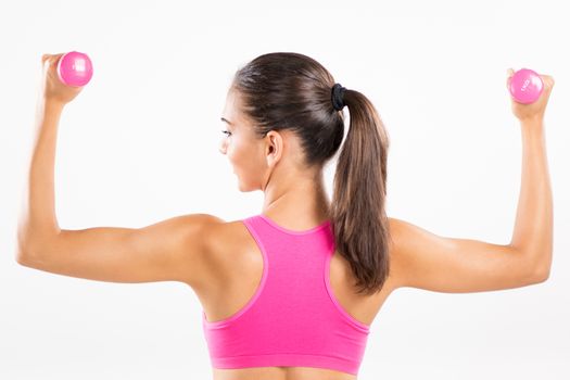 Portrait of a young beautiful woman exercising with dumbbells. She is practicing upper body muscle group. Rear View.