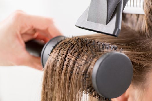 Drying long brown hair with hair dryer and round brush. Close-up.