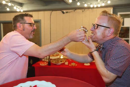 Gay male couple share bacon cupcake at their wedding 