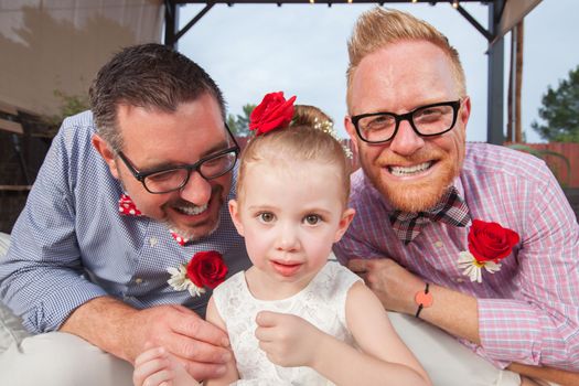 Smiling gay couple with daughter sitting outdoors