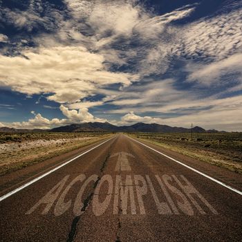 Conceptual image of desert road with the word accomplish and arrow