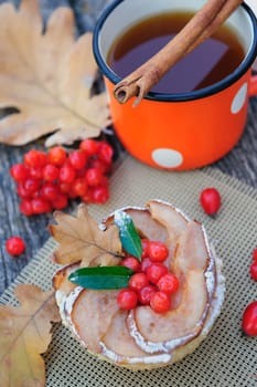 Romantic autumn still life with basket cake, cup of tea, rowan berries and leaves at wooden board