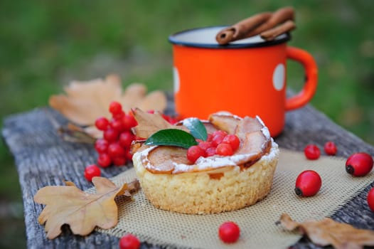 Romantic autumn still life with basket cake, cup of tea, rowan berries and leaves at wooden board