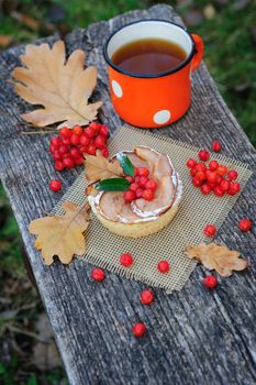 Romantic autumn still life with basket cake, cup of tea, rowan berries and leaves at wooden board