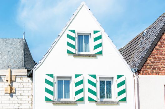 White House front gable with shutters in white green. Blue sky with clouds.
