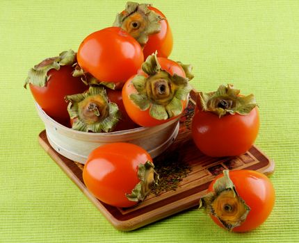 Delicious Raw Persimmon in Wooden Bowl closeup on Green Textile Napkin background
