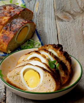 Slices of Delicious Homemade Meatloaf Stuffed with Boiled Eggs and Greens  in Two Bowl closeup on Rustic Wooden background