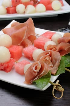 Appetizer of ham with melon and watermelon and basil on a skewer