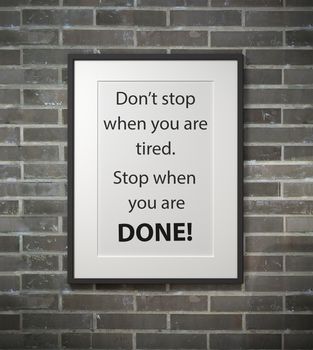 Inspirational quote on picture frame over a dirty brick wall. DON'T STOP WHEN YOU ARE TIRED. STOP WHEN YOU ARE DONE.