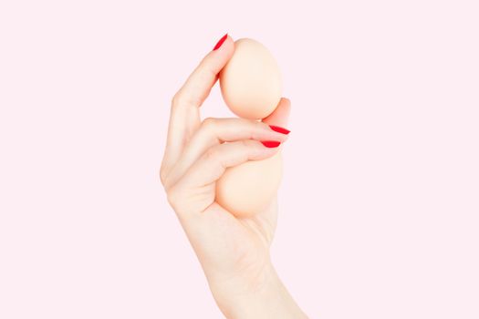 Female hand with red fingernails holding two eggs isolated on pink background. Feminism, emancipation, provocation and relationship problems.