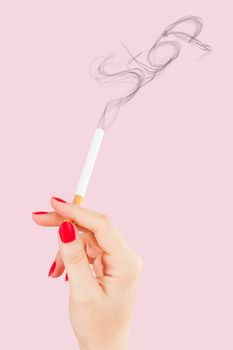 Female hand holding cigarette, smoke forming the word stop isolated on pink background. Feminine tobacco abuse.