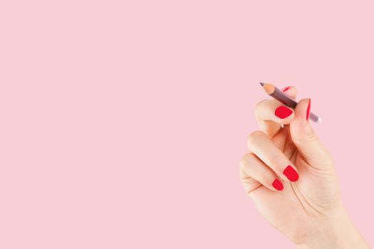 Female hand with red fingernails holding a pencil isolated on pink background. Creativity and copy writing, teaching and learning. 