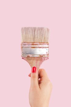 Female hand with red fingernails holding paintbrush isolated on pink background. Creative painting. 