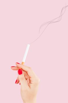Female hand holding cigarette isolated on pink background. Feminine tobacco abuse.