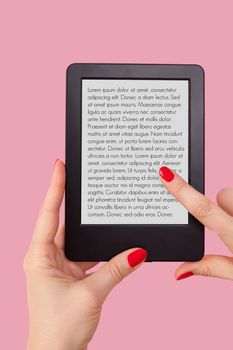 Female hand holding e reader isolated on pink background. Reading, education and learning concept. 