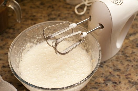 Mixing batter for baking in a large bowl on an electric mixer fitted with a whisk, close up view