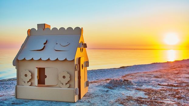 Toy house made of corrugated cardboard in the sea coast at sunset. The concept of eco-estate