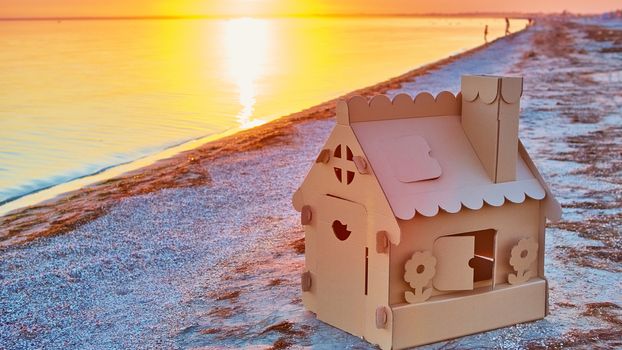 Toy house made of corrugated cardboard in the sea coast at sunset. The concept of eco-estate